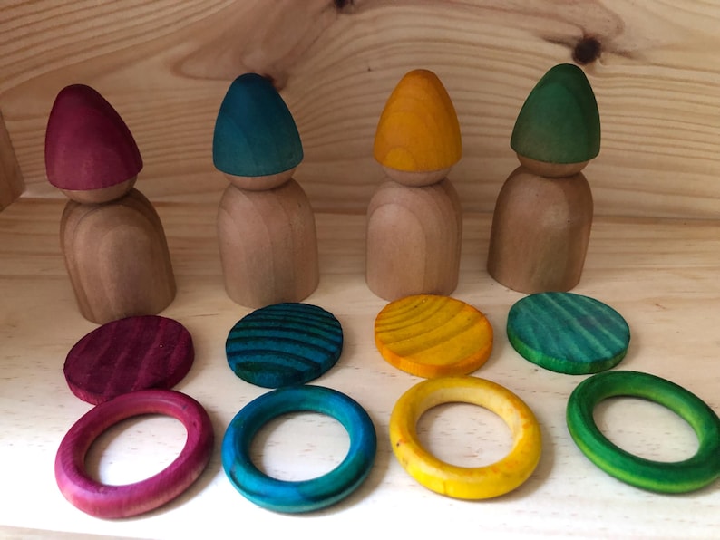 Peut inclure: Ensemble de jouets en bois comprenant quatre poup&eacute;es en bois avec des chapeaux coniques color&eacute;s en rouge, bleu sarcelle, jaune et vert. L'ensemble comprend des disques et des anneaux en bois de couleur assortie.