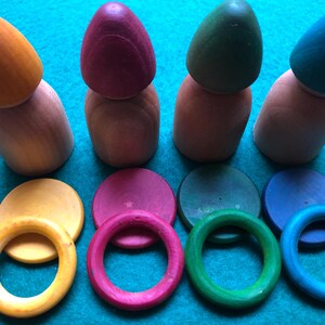 Peut inclure: Jeu de construction en bois avec quatre poup&eacute;es en forme de quilles de couleurs orange, bordeaux, vert et bleu sarcelle. Comprend des anneaux et des disques de couleurs assorties. Un jouet &eacute;ducatif color&eacute; pour les tout-petits.