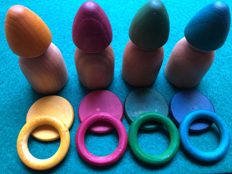 Peut inclure: Jeu de construction en bois avec quatre poup&eacute;es en forme de quilles de couleurs orange, bordeaux, vert et bleu sarcelle. Comprend des anneaux et des disques de couleurs assorties. Un jouet &eacute;ducatif color&eacute; pour les tout-petits.