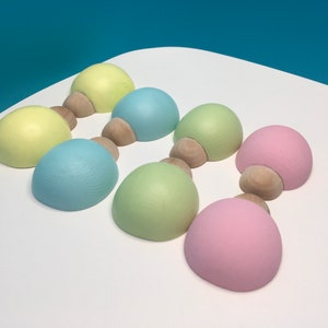 May include: Seven pastel-coloured wooden decorative objects. Each object has a rounded top in shades of yellow, blue, green, and pink, connected to a small, natural wood base. The objects are arranged on a white surface.