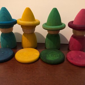 Peut inclure: Quatre poup&eacute;es en bois avec des chapeaux coniques et des bases circulaires assorties. Les poup&eacute;es sont peintes en turquoise, jaune, vert et rose. Les bases sont de la m&ecirc;me couleur que les chapeaux. Les poup&eacute;es sont sur une surface marron.
