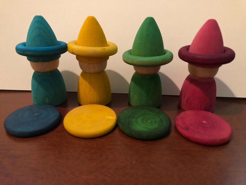 Peut inclure: Quatre poup&eacute;es en bois avec des chapeaux coniques et des bases circulaires assorties. Les poup&eacute;es sont peintes en turquoise, jaune, vert et rose. Les bases sont de la m&ecirc;me couleur que les chapeaux. Les poup&eacute;es sont sur une surface marron.
