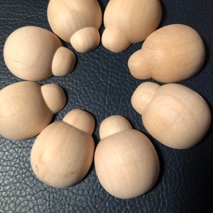 May include: Seven unfinished wooden mushroom-shaped knobs arranged in a circle. Each knob has a rounded top and a smaller, bulbous base. The wood has a light, natural colour, and the knobs are set against a dark blue textured surface.