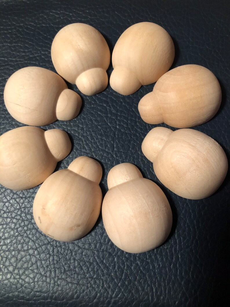May include: Seven unfinished wooden mushroom-shaped knobs arranged in a circle. Each knob has a rounded top and a smaller, bulbous base. The wood has a light, natural colour, and the knobs are set against a dark blue textured surface.