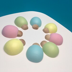 May include: Eight pastel-coloured, oval-shaped decorative objects arranged in a circle. Each has a light-coloured, rounded top and a small, wooden base. The colours include pink, yellow, green, and blue.