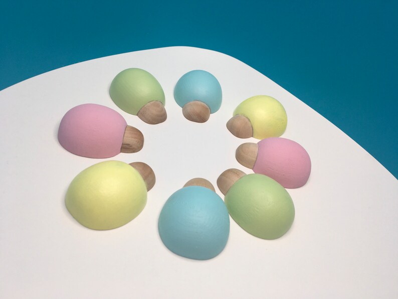 May include: Eight pastel-coloured, oval-shaped decorative objects arranged in a circle. Each has a light-coloured, rounded top and a small, wooden base. The colours include pink, yellow, green, and blue.