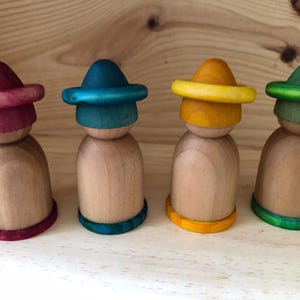 Peut inclure: Quatre poup&eacute;es en bois avec des chapeaux et des bases color&eacute;s. Les chapeaux sont peints dans des tons de rouge, de bleu, de jaune et de vert. Les poup&eacute;es sont en bois naturel et sont sur une surface en bois.