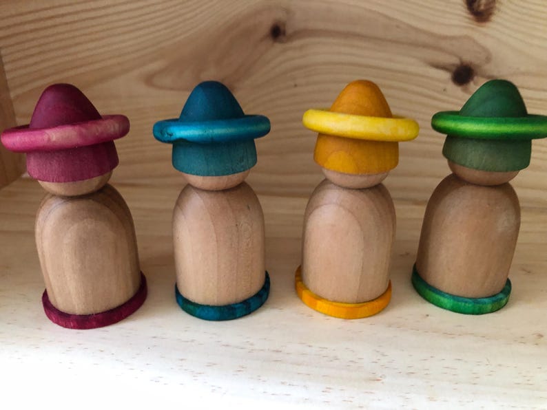 Peut inclure: Quatre poup&eacute;es en bois avec des chapeaux et des bases color&eacute;s. Les chapeaux sont peints dans des tons de rouge, de bleu, de jaune et de vert. Les poup&eacute;es sont en bois naturel et sont sur une surface en bois.
