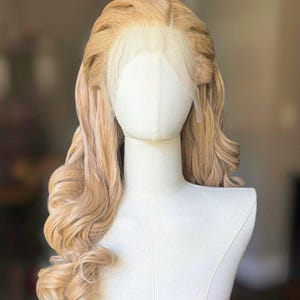 May include: A blonde wig with long, wavy curls styled on a mannequin head. The wig features a lace front and a light brown colour with highlights. The hair is styled with volume at the crown and cascading curls.