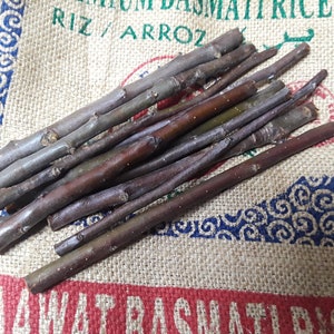 May include: A pile of brown and purple sticks, likely for crafts or decor, on a burlap background with blue and white patterned text.