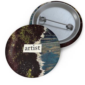 Könnte beinhalten: Ein runder Knopf mit einem abstrakten Design in Dunkelblau, Grün und Braun. Das Wort "Künstler" ist auf einem weißen Etikett in der Mitte des Knopfes gedruckt.