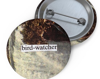 Pode incluir: Um botão redondo com uma imagem vintage de uma cena de floresta e o texto "bird-watcher" impresso nele.