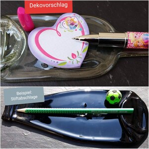 Könnte beinhalten: Zwei Beispiele, wie man eine recycelte Glasflasche als dekorativen Stifthalter verwenden kann. Das erste Beispiel zeigt eine klare Glasflasche mit einem herzförmigen Haftnotiz und einem Stift mit einem rosa-weißen Design. Das zweite Beispiel zeigt eine schwarze Glasflasche mit einem grünen Bleistift und einem grünen Fußball.