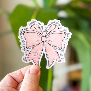 May include: A pink bow with a cross in the center and the text "She is clothed with strength and dignity, and she laughs without fear of the future. Proverbs 31:25"