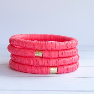 May include: Four stacked pink bracelets with gold accents. The bracelets are made of round beads.