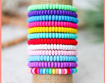 May include: A stack of colorful silicone beaded bracelets in various colors, including green, purple, pink, yellow, blue, and white. The bracelets are stacked on a brown burlap stand. "Lots of beautiful colors to choose from. These are great for gifts for teachers, friends, your BFF, kids and moms alike. ...This listing is for one bracelet."