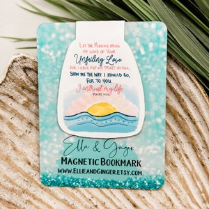May include: A blue and white magnetic bookmark with a watercolor illustration of a sunrise over the ocean. The bookmark features the text "Let the morning bring me word of your Unfailing Love, for I have put my trust in you. Show me the way I should go, for to you I entrust my life. Psalms 143:8."  The bookmark is designed by Elle & Ginger.