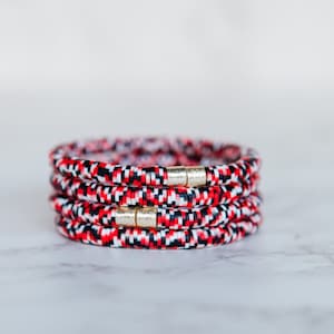 May include: Four stacked bracelets made of red, black, and white beads with gold accents.