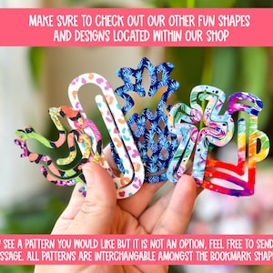 May include: Five colorful paper clip bookmarks in different shapes, including a pineapple, a bird, and a flower. The bookmarks are made of paper and have a variety of patterns. The text on the image reads: "Make sure to check out our other fun shapes and designs located within our shop. If you see a pattern you would like but it is not an option, feel free to send me a message. All patterns are interchangeable amongst the bookmark shapes."
