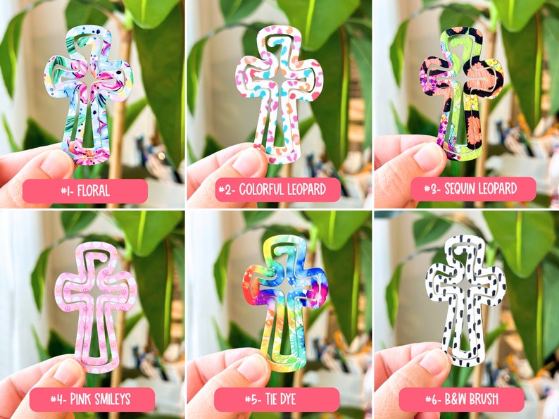 May include: Six different cross-shaped hair clips with various patterns, including floral, leopard print, tie-dye, and smiley faces. The clips are all made of plastic and have a white background.