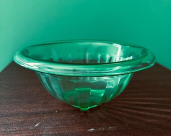 May include: A green glass bowl with a fluted design. The bowl has a wide rim and a rounded bottom.