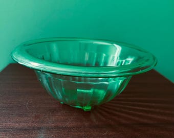 May include: A green glass bowl with a fluted design. The bowl is empty and sitting on a dark brown wooden surface.
