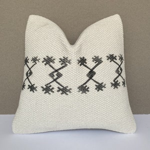 Könnte beinhalten: Ein weißes Kissen mit einem schwarzen geometrischen Muster am Rand.