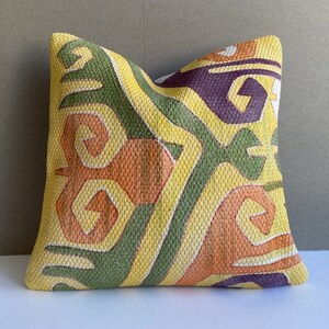 Könnte beinhalten: Ein gelbes, grünes, oranges und violettes Kissen mit geometrischem Muster.