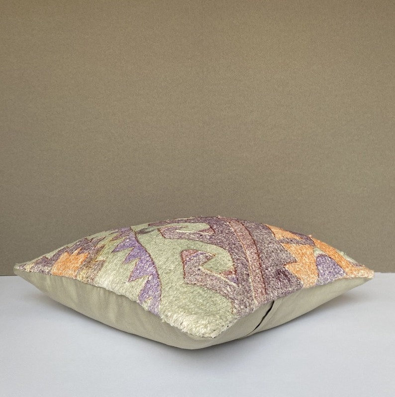 Peut inclure: Un coussin d&eacute;coratif avec un fond beige et un motif g&eacute;om&eacute;trique color&eacute; dans les tons de violet, orange et vert.