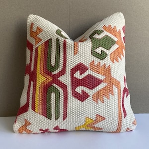 Könnte beinhalten: Ein weißes Kissen mit einem geometrischen Muster in Rot-, Orange-, Gelb- und Grüntönen. Das Muster ist in den Stoff eingewebt und hat eine leicht erhabene Textur.