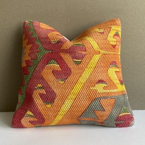 Könnte beinhalten: Ein farbenfrohes Kissen mit einem geometrischen Muster in Rot-, Orange-, Gelb- und Grüntönen. Das Kissen ist aus einem gewebten Stoff mit einer strukturierten Oberfläche.