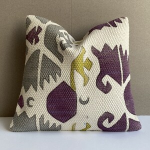 Könnte beinhalten: Ein weißes Kissen mit einem geometrischen Muster in den Farben Lila, Grau und Gelb.