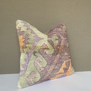 Peut inclure: Un coussin d&eacute;coratif avec un motif g&eacute;om&eacute;trique dans des tons de violet, vert et orange. Le coussin est fait d'un tissu doux et textur&eacute;.