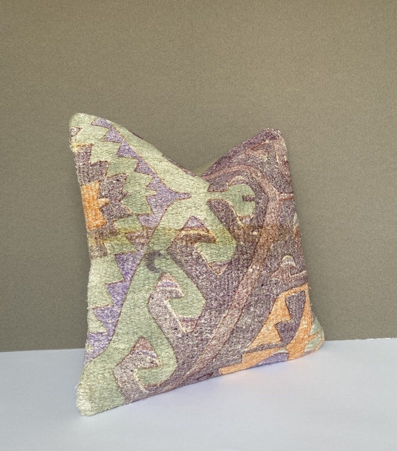 Peut inclure: Un coussin d&eacute;coratif avec un motif g&eacute;om&eacute;trique dans des tons de violet, vert et orange. Le coussin est fait d'un tissu doux et textur&eacute;.
