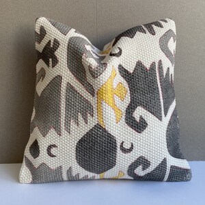 Könnte beinhalten: Ein weißes Kissen mit einem geometrischen Muster in Grautönen und Gelb. Das Muster besteht aus abstrakten Formen und Linien.