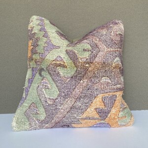 Peut inclure: Un coussin d&eacute;coratif avec un motif g&eacute;om&eacute;trique dans des tons de vert, violet et orange. Le coussin est fait d'un tissu doux et textur&eacute;.