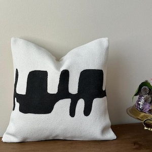 May include: White throw pillow with a black abstract design. The design resembles dripping paint.
