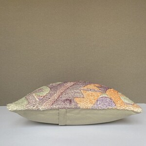 Peut inclure: Un coussin rectangulaire avec une housse en tissu beige et un motif g&eacute;om&eacute;trique color&eacute; sur le devant. Le motif pr&eacute;sente des nuances de violet, d'orange et de vert.