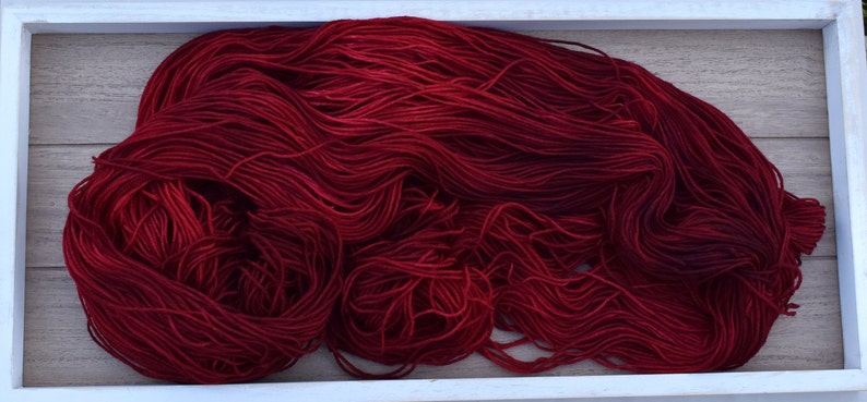 Puede incluir: Una madeja grande y suelta de hilo rojo carmes&iacute; profundo con una textura suave y ligeramente lustrosa. El hilo se compone de muchas hebras finas y continuas agrupadas en un arreglo org&aacute;nico y enredado, mostrando un color rico.