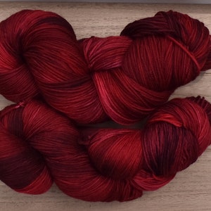 Puede incluir: Dos madejas de hilo te&ntilde;ido a mano con una paleta de colores variados y profundos en carmes&iacute;, burdeos y rojo vino oscuro. Los haces de fibra trenzados muestran una textura suave y lustrosa con sutiles cambios tonales.
