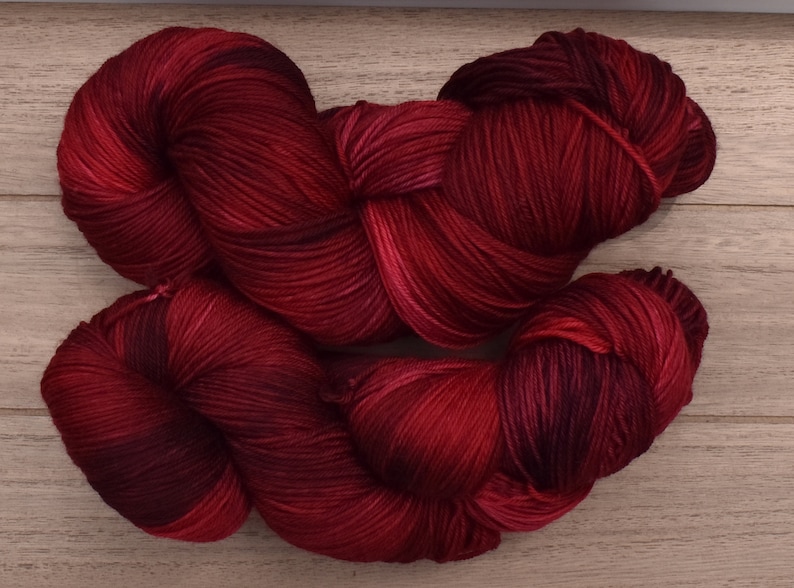 Puede incluir: Dos madejas de hilo te&ntilde;ido a mano con una paleta de colores variados y profundos en carmes&iacute;, burdeos y rojo vino oscuro. Los haces de fibra trenzados muestran una textura suave y lustrosa con sutiles cambios tonales.