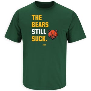 May include: Green t-shirt with the text "THE BEARS STILL SUCK." in yellow and white, and a cartoon bear head graphic in orange and brown. The shirt is a crew neck style.