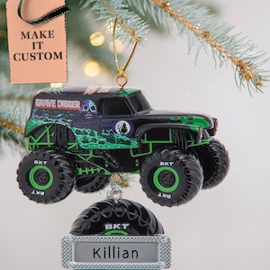 May include: A black and green monster truck ornament with the words "GRAVE DIGGER" on the side. The ornament has large black tires with the letters "BKT" on them. A personalized ornament below reads "Killian". A tag reads "MAKE IT CUSTOM".