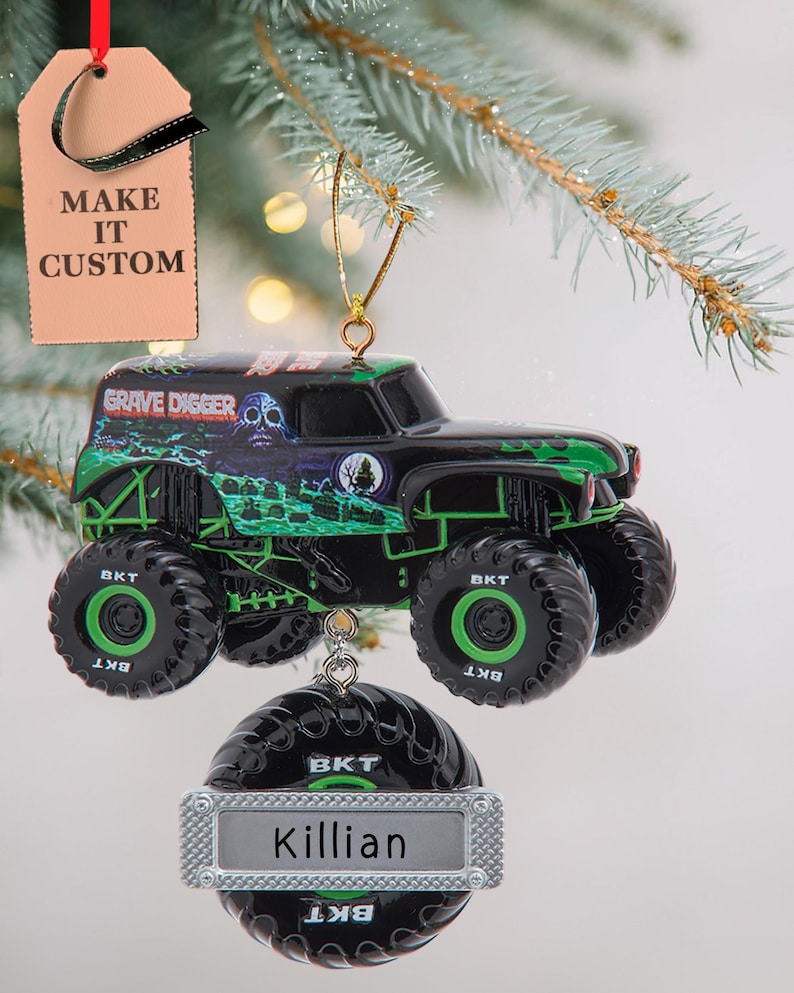 May include: A black and green monster truck ornament with the words "GRAVE DIGGER" on the side. The ornament has large black tires with the letters "BKT" on them. A personalized ornament below reads "Killian". A tag reads "MAKE IT CUSTOM".