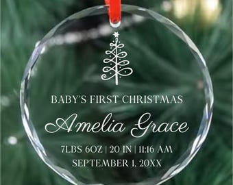 May include: A clear, faceted glass Christmas ornament with a red ribbon. The ornament features the text "BABY'S FIRST CHRISTMAS" and the name "Amelia Grace". It also includes birth details: 7lbs 6oz, 20 inches, and the date and time.