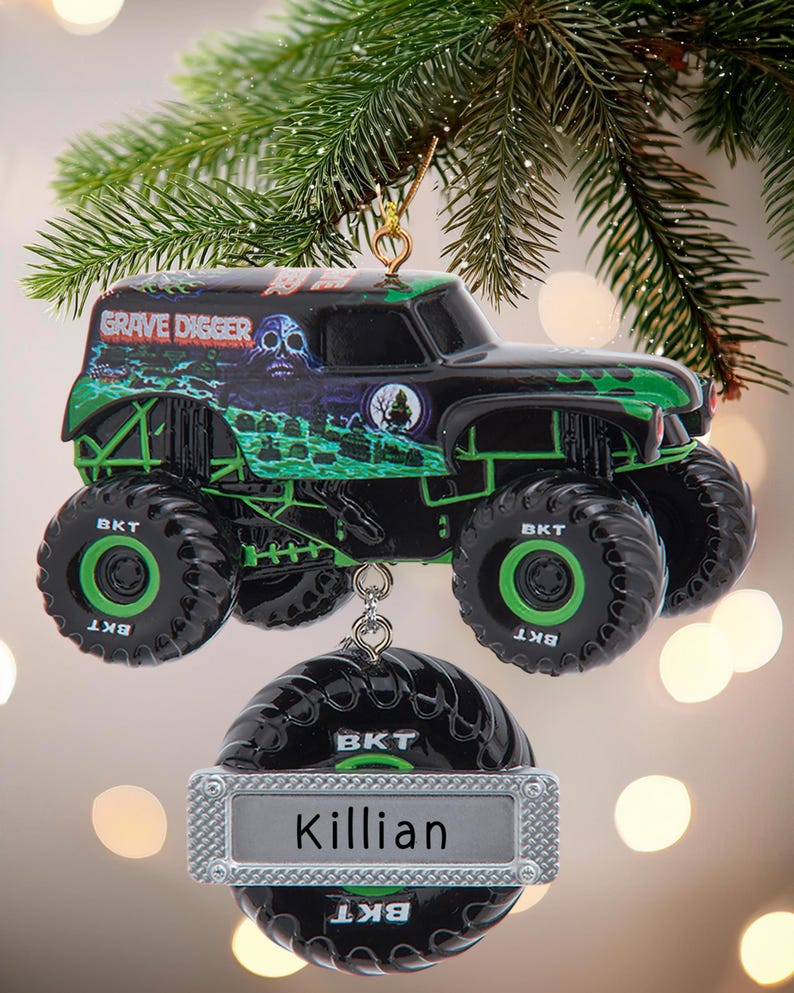 May include: Black and green Grave Digger monster truck ornament with the name "Killian" on a silver tag. The truck has large black tires with green accents and the text "BKT". The ornament hangs from a gold-colored hook.