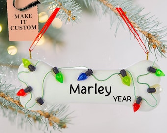 May include: White ceramic dog bone ornament with colorful light bulbs and the name "Marley" and the word "YEAR" on it.