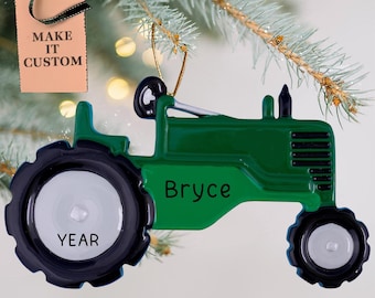 May include: Green tractor Christmas ornament with a black tyre and a white wheel. The ornament has the name "Bryce" and the word "YEAR" on it.