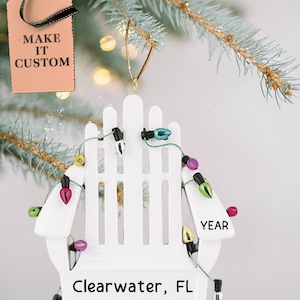 May include: White wooden chair ornament with string lights and the text "Clearwater, FL" and "YEAR" on it.