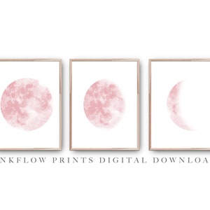 May include: Set of three digital prints featuring pink watercolor moons in different phases. The prints are framed in a light wood frame and have a white background.